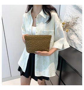 Detail view of brown textured clutch bag with 3D floral pattern held by a model