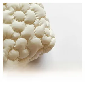 Macro detail of white quilted fabric featuring delicate floral stitching and texture