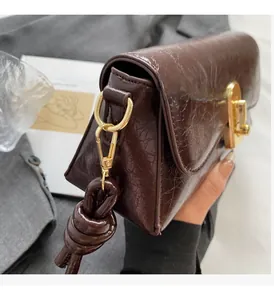 Gros plan du sac bandoulière marron brillant avec boucle dorée et détail de nœud