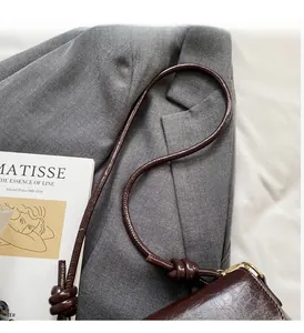 Détail du sac bandoulière marron foncé vintage avec noeud sur un costume gris