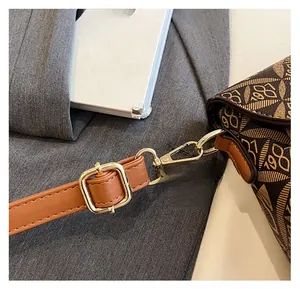 Dettaglio del gancio in metallo dorato e della tracolla stampata marrone della borsa