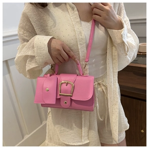 Detailed view of pink mini handbag with golden buckle held by a model in casual outfit