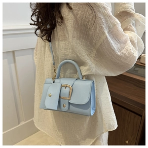 Detail of light blue crossbody bag featuring a golden buckle and small coin purse attachment