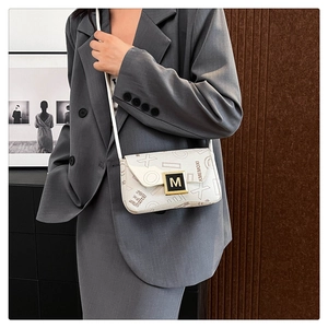 Detail of white leather shoulder bag with gold M-logo buckle worn with a grey blazer