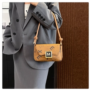 Detail of caramel underarm bag featuring monogram print and golden M buckle on flap