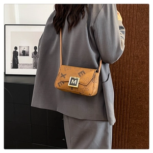 Close-up of tan crossbody bag with letter print and golden M-lock worn by a model