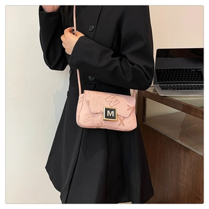 Detail view of pink textured leather crossbody bag with gold buckle on black blazer