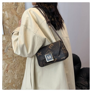 Detail of vintage patterned crossbody bag featuring silver square buckle with letter M logo