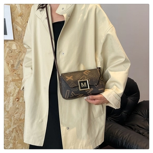 Detail of vintage brown printed crossbody bag with golden M metal buckle on trench coat
