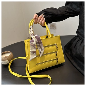 Detail of bright yellow PU leather bag featuring triple zipper design and silk scarf handle