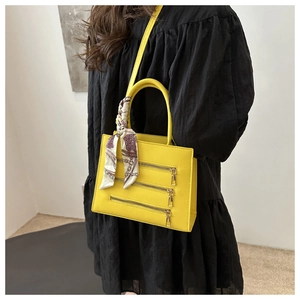 Detail of bright yellow crossbody bag with decorative zippers and silk scarf handle accent