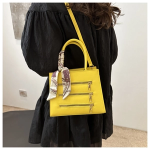 Close-up of yellow PU leather square bag with decorative zippers and silk scarf on a model