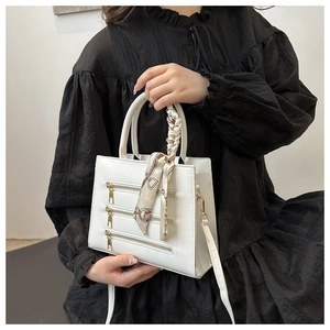 Detail of white crossbody bag with triple gold zippers and silk scarf handle accent