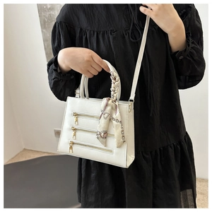 Close-up of a white leather bag featuring three gold zippers and a silk scarf handle