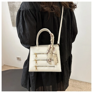 Close-up of white crossbody bag with gold zippers and silk scarf on a black dress