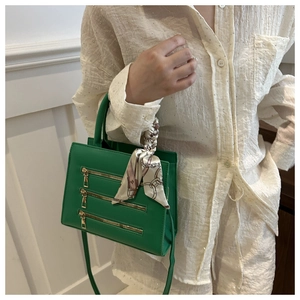 Close-up of green handbag with gold zippers and decorative silk scarf on the handle