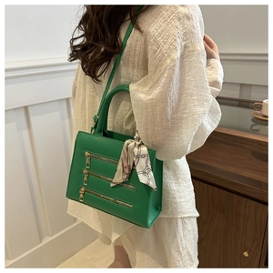 Detail of green crossbody bag with triple gold zipper design and elegant scarf handle