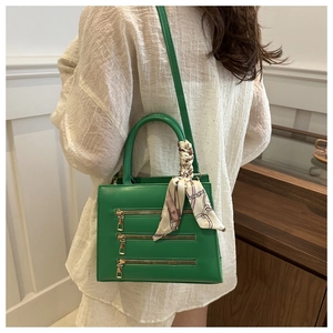 Detail of green square bag with triple zippers, silk scarf handle, and long shoulder strap
