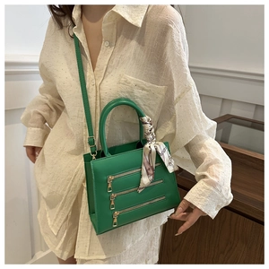 Detail of green crossbody bag with triple zippers and decorative scarf on handle