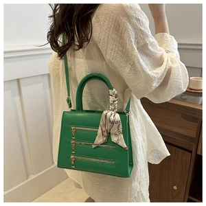 Detail shot of bright green crossbody bag with gold zippers and printed silk scarf handle