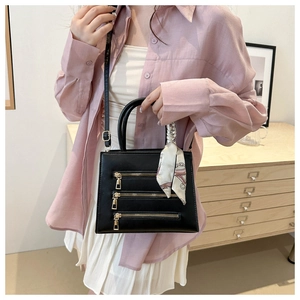 Detail view of black crossbody bag with triple gold zippers and silk scarf handle decor