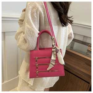 Detail of rose pink square handbag with gold zippers and silk scarf on a white dress