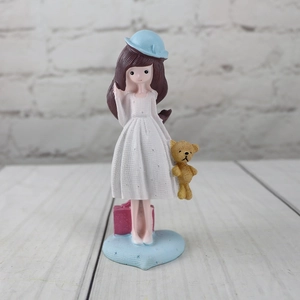 Detail of girl figurine with teddy bear and pink suitcase on heart-shaped base