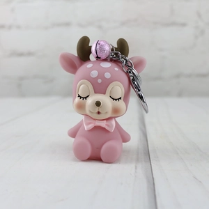 Pink cartoon deer keychain with a matching bell and silver ring on a light wood background