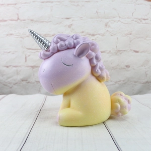 Detalle de hucha de unicornio con degradado púrpura y amarillo y un cuerno plateado