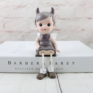 Close-up of a resin angel figurine sitting on a book edge with purple horns and wings