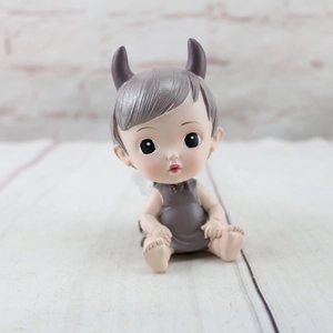 Close-up of a resin angel figurine with grey horns and white wings on a wooden desk
