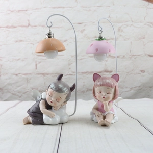 Close-up of resin angel figurines with metal hooks and glowing fruit-shaped LED lamps