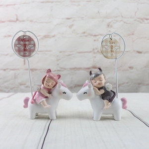 Close-up of resin angel figurines on unicorns with calendar cards for Monday and Saturday