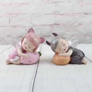 Detail of resin angel and devil baby figurines resting on fruit and strawberry bases