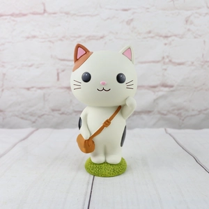 Close-up of a cute cartoon cat figurine with a brown bag on a green grass base