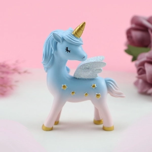Close-up of a gradient blue resin unicorn cake topper with golden stars and glittery wings