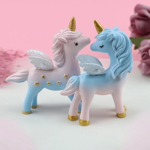 Close-up of resin unicorn figurines with golden horns and sparkling wings on pink background