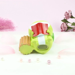 Close-up of cute green frog night light figurine reading a red book on a wooden base