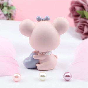 Détail du dos d'une figurine de souris rose avec un nœud violet et un col en dentelle