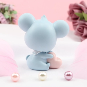 Détail d'une figurine bleue tenant un cœur rose sur fond décoratif avec des plumes