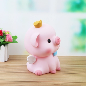 Hucha de cerdito rosa con corona dorada y alas decorativas sobre mesa de madera