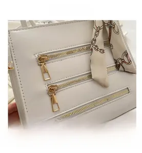 Detail view of white square handbag with three gold decorative zippers and printed silk scarf