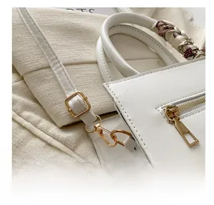 Close-up of white leather handbag featuring gold hardware and a decorative silk scarf