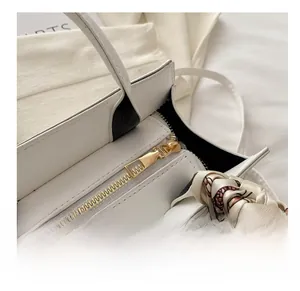 Detail of smooth gold metal zipper and silk scarf wrapped on white leather handbag