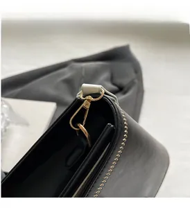 Detailed close-up of golden metal clasp and leaf-pattern embroidery on black leather bag