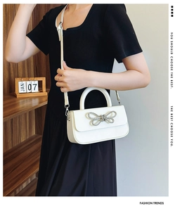 Close-up of elegant white leather handbag with sparkling silver rhinestone bow detail