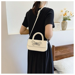 Close-up of white leather handbag featuring a sparkling silver bow and adjustable strap