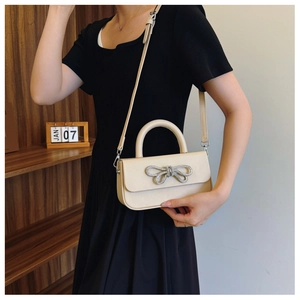 Detailed view of cream bow square bag with diamond embellishment worn by a model