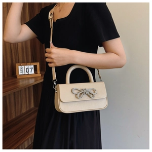Detail of a beige PU leather crossbody bag featuring a sparkling rhinestone bow buckle
