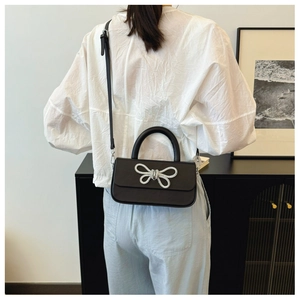 Modern black box bag with silver bow accent worn as a crossbody by a model in a minimal room
